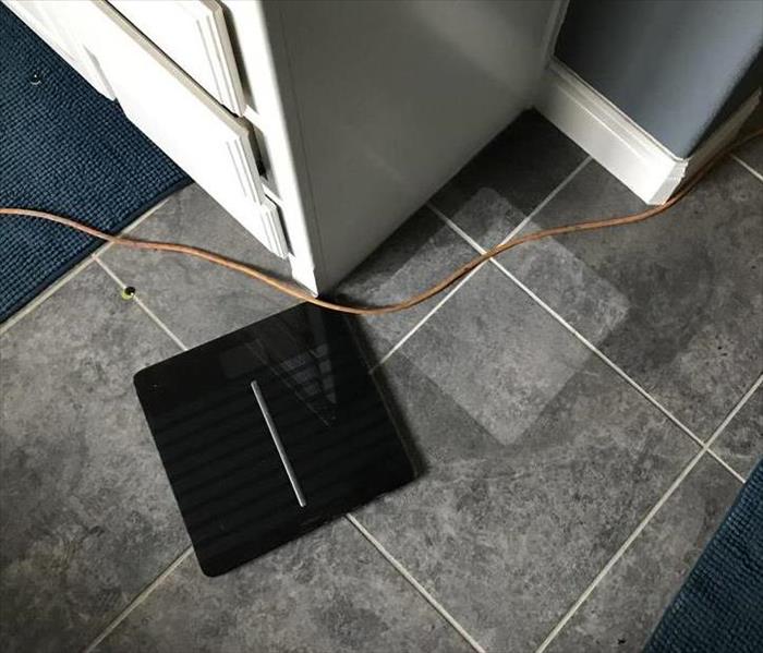 Bathroom scale on a floor next to the outline of the shape of it in soot.