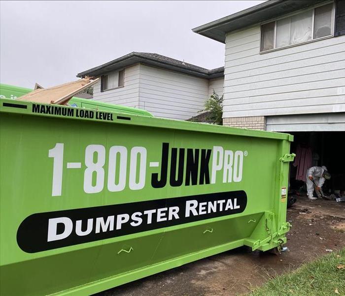 Green "1-800-JUNKPRO" dumpster in the driveway of a residence.