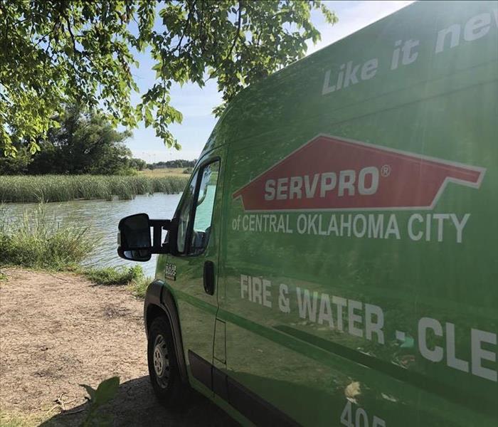 Green SERVPRO van parked in front of green foliage and a small body of water.