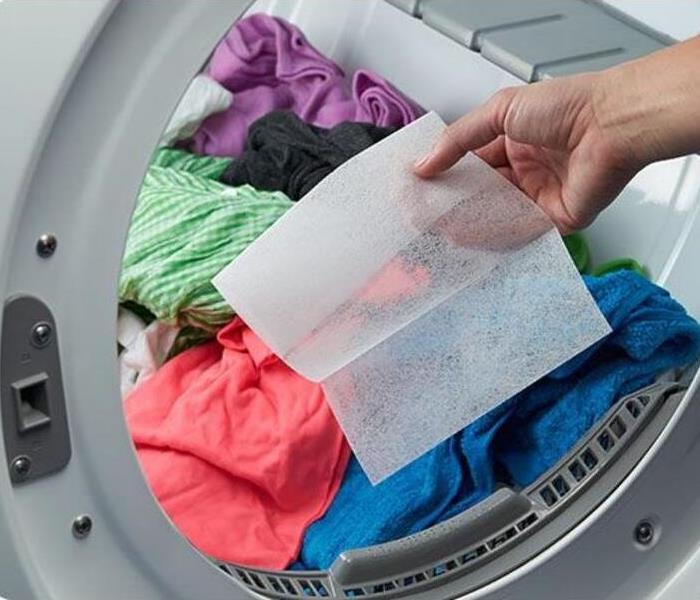 Pile of clothes in a dryer with a dryer sheet being put in the dryer by a female’s hand. 