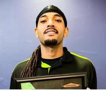 A man with long braids and a durag smiles at the camera